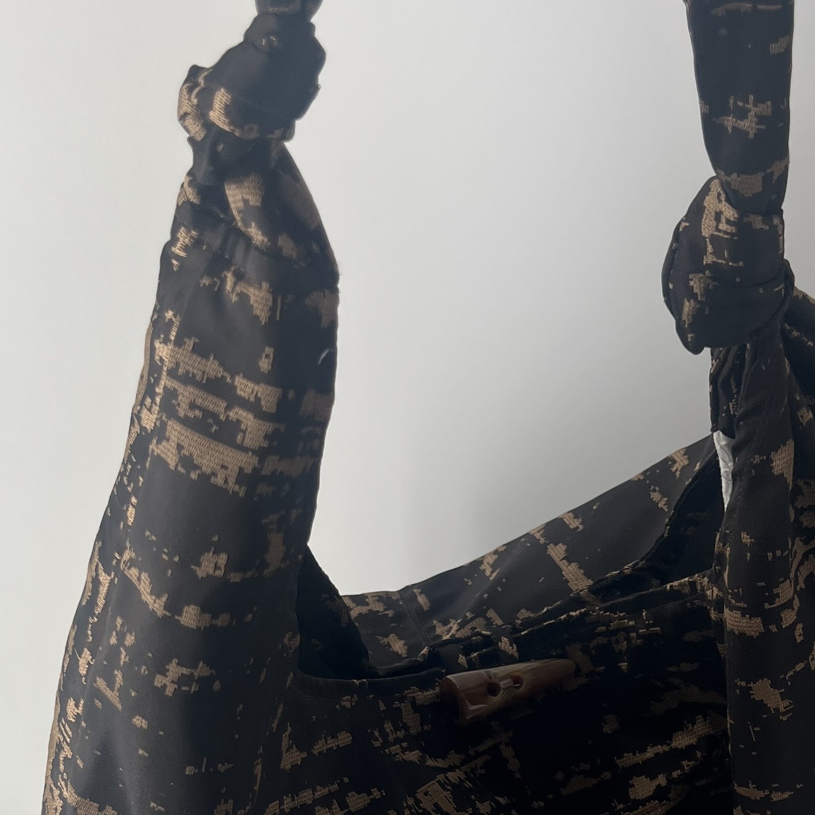 Black and gold brocade knot bag with a hand-tied closure.