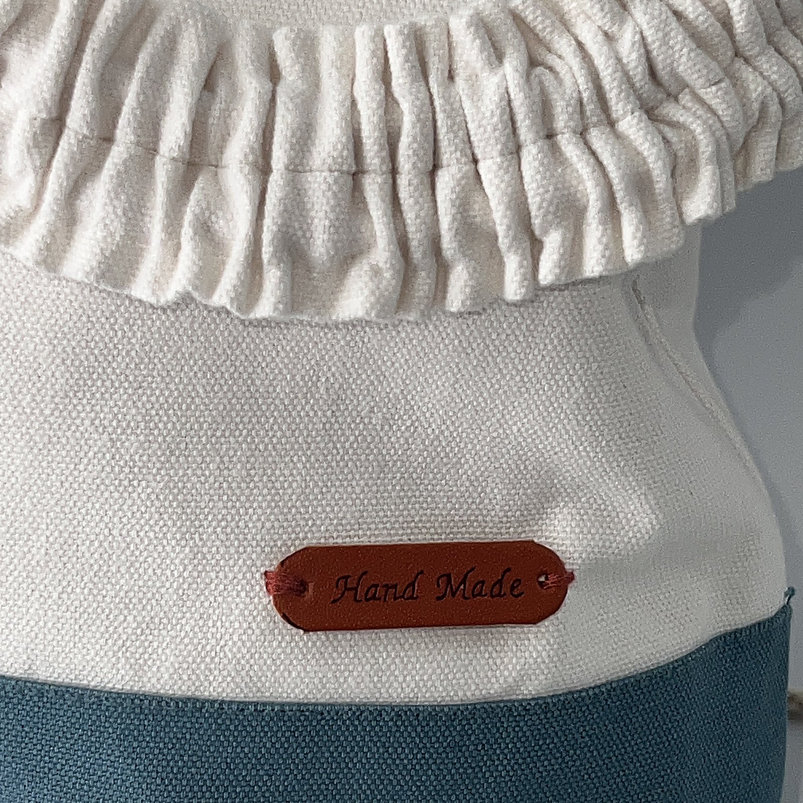 White canvas crossbody with a teal base, drawstring top and small leather tag.