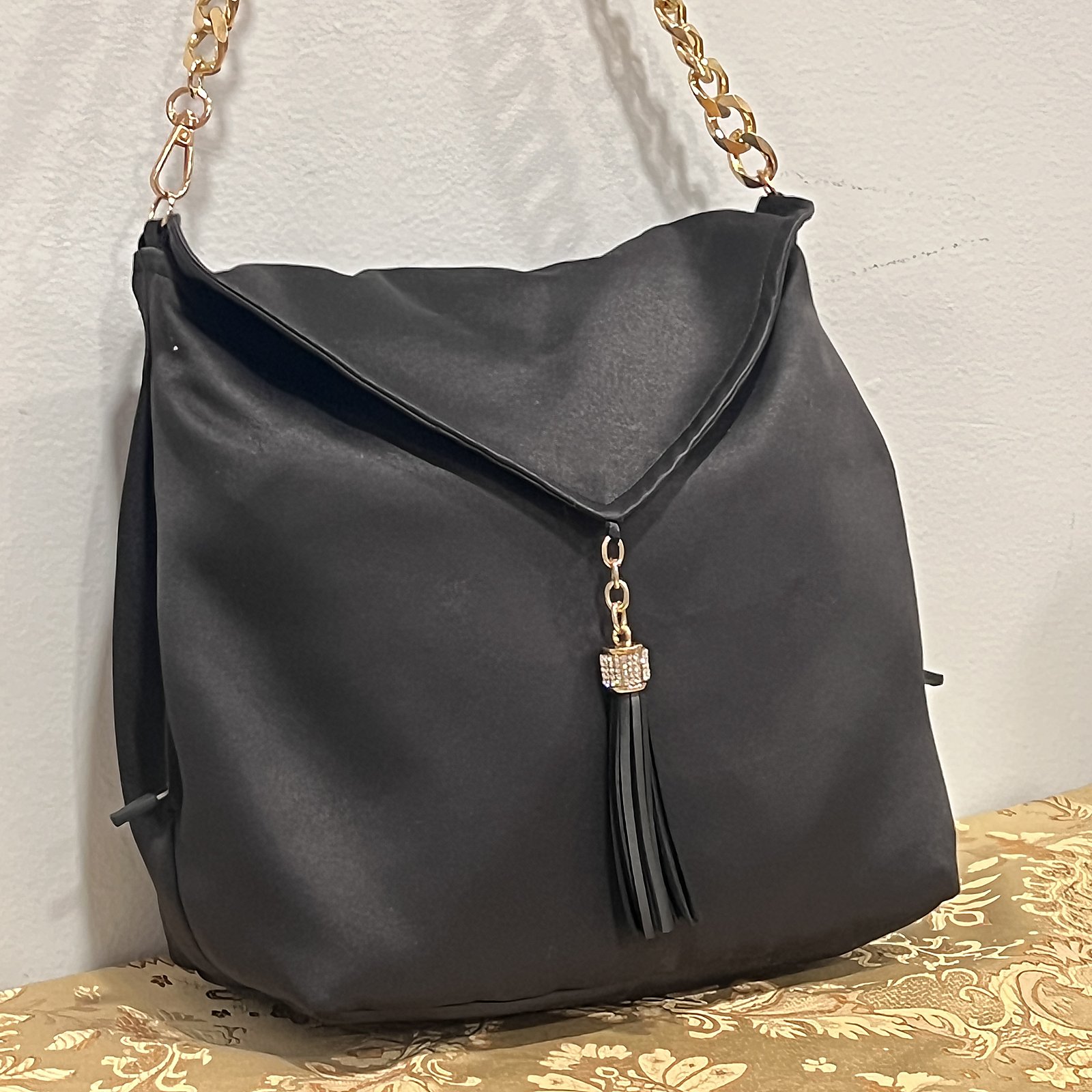 Black satin evening bag with gold chain strap and leather tassel.