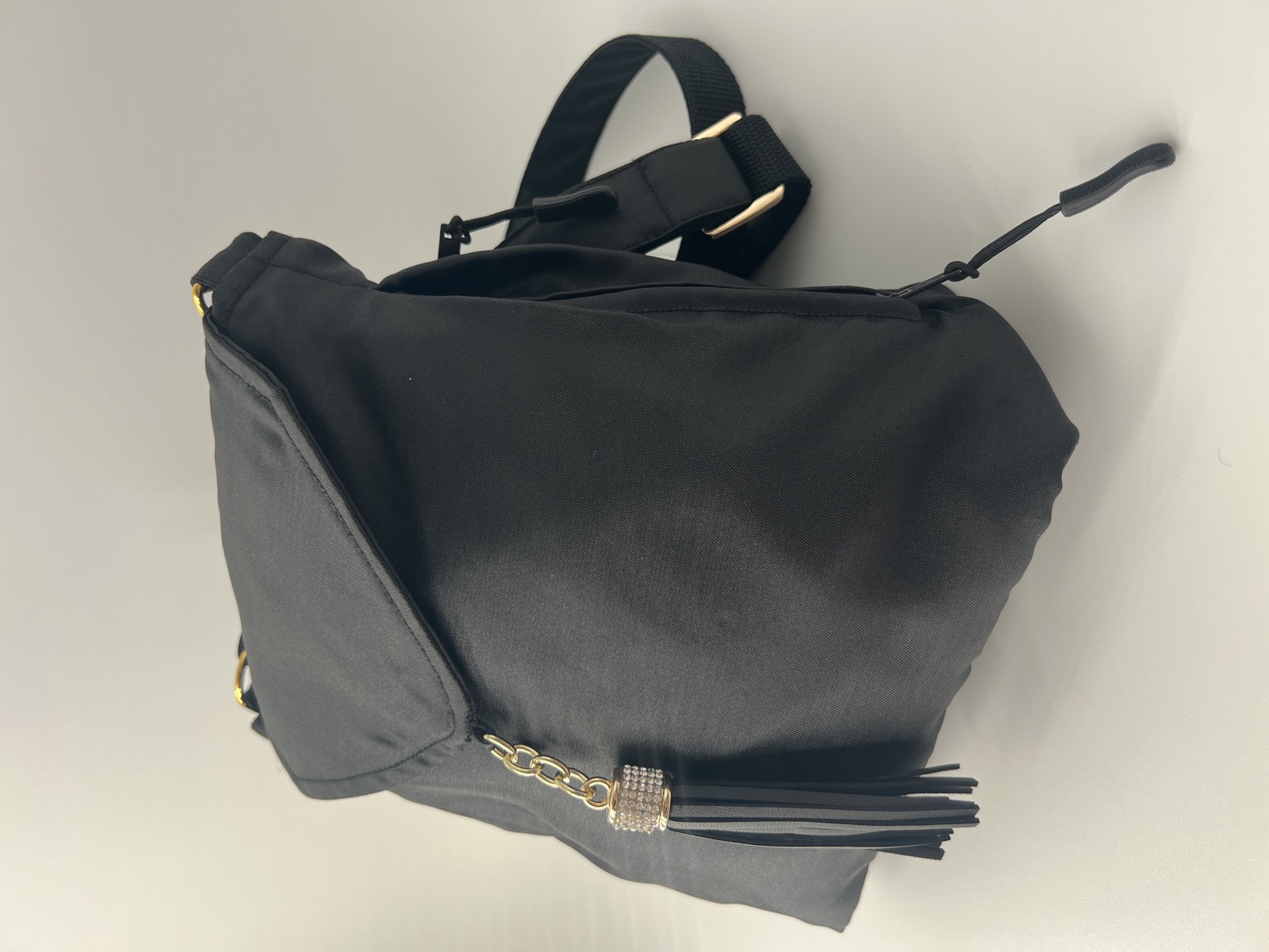 Black satin envelope crossbody with a crystal-and-leather tassel on a gold chain.